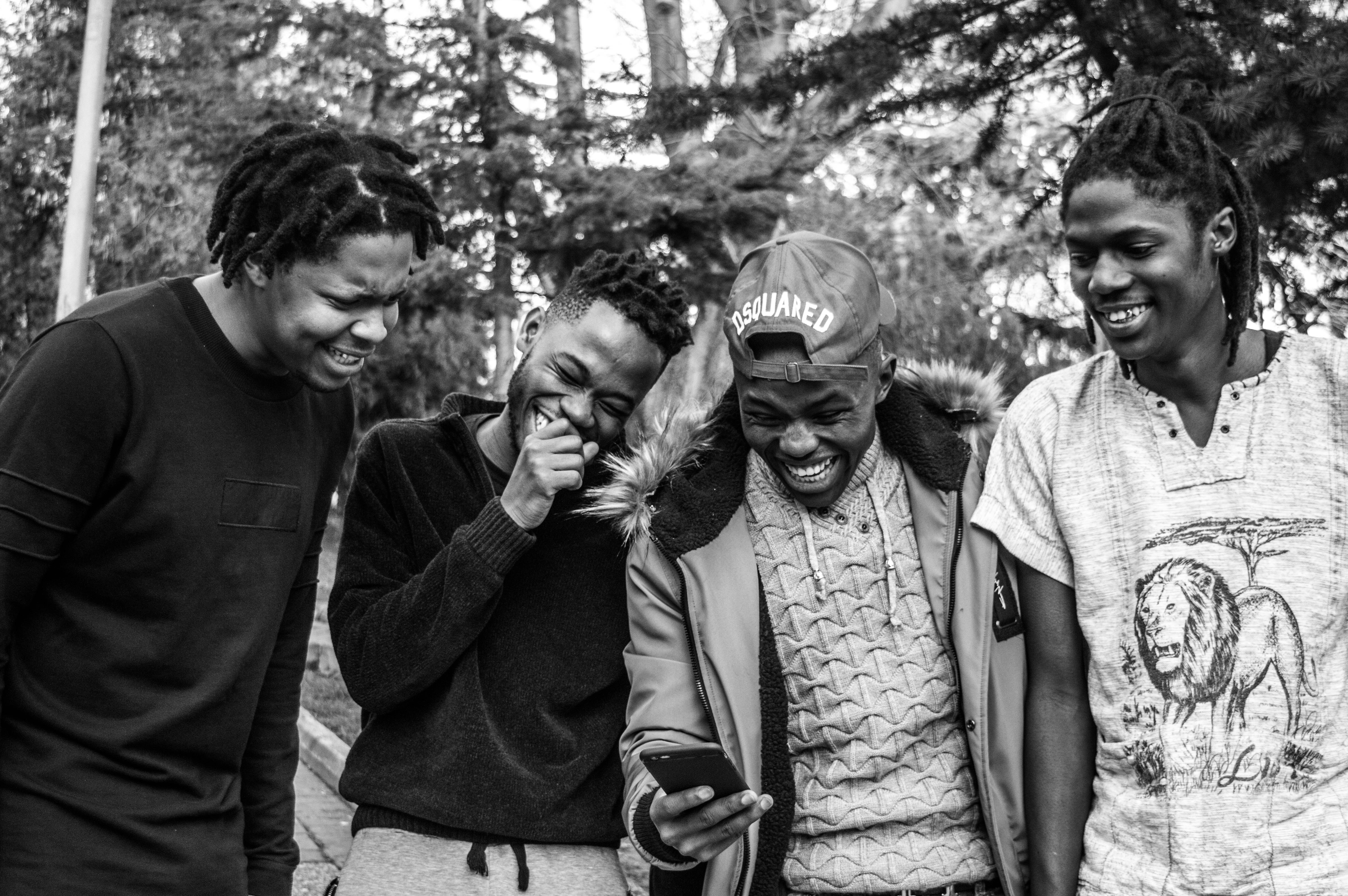 four boys laughing and sitting on grass during daytime